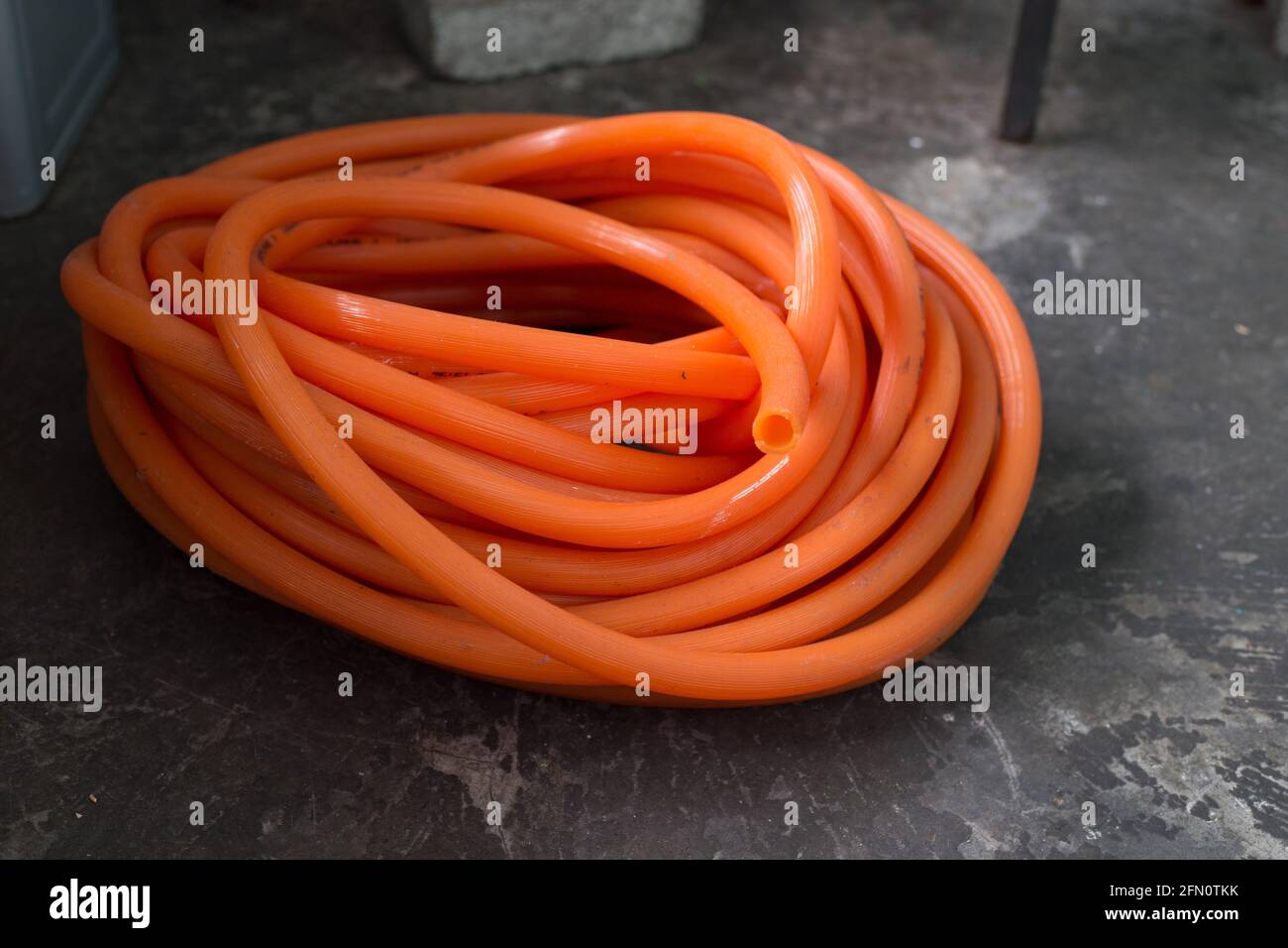 Colpo di closeup del tubo di gomma arancione arrotolato sulla superficie di calcestruzzo Foto Stock