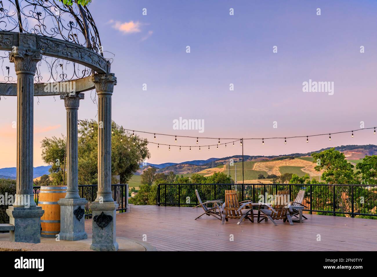 Sedie all'aperto e tavolo su un ponte di legno al tramonto in primavera con viti e colline sullo sfondo, Napa Valley, California USA Foto Stock