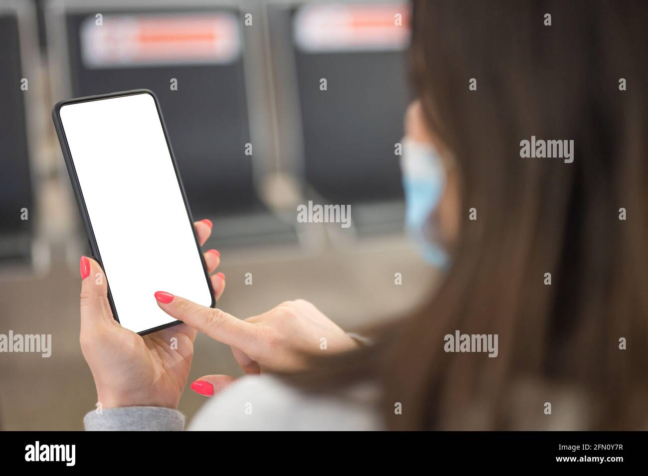 Immagine mockup di mani femminili che tengono nero telefono cellulare con schermo bianco vuoto sopra bordo di volo nel terminale dell'aeroporto. Donna che usa il cellulare w Foto Stock