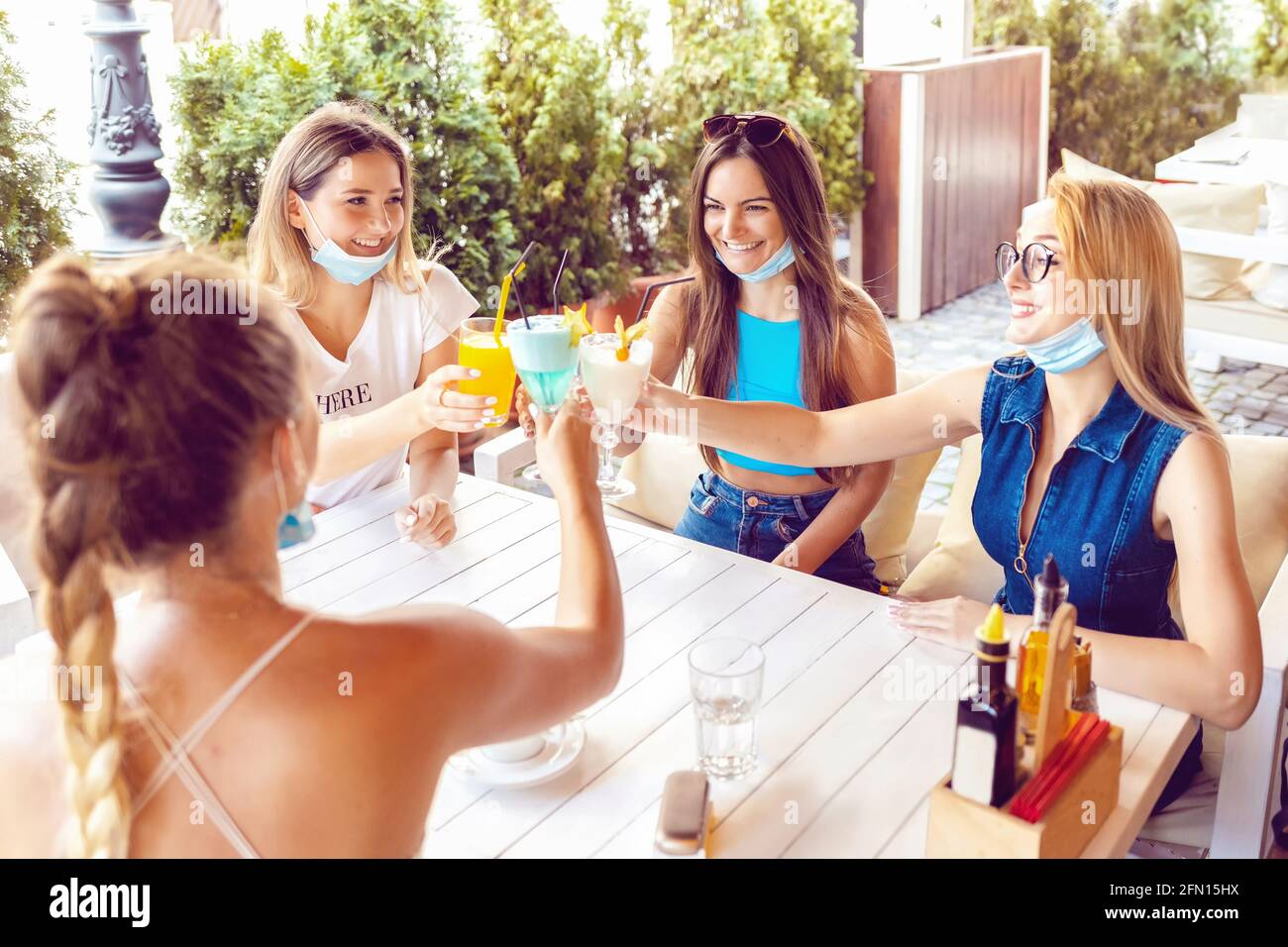 Felici le giovani donne con maschere aperte che bevono cocktail al pub Foto Stock