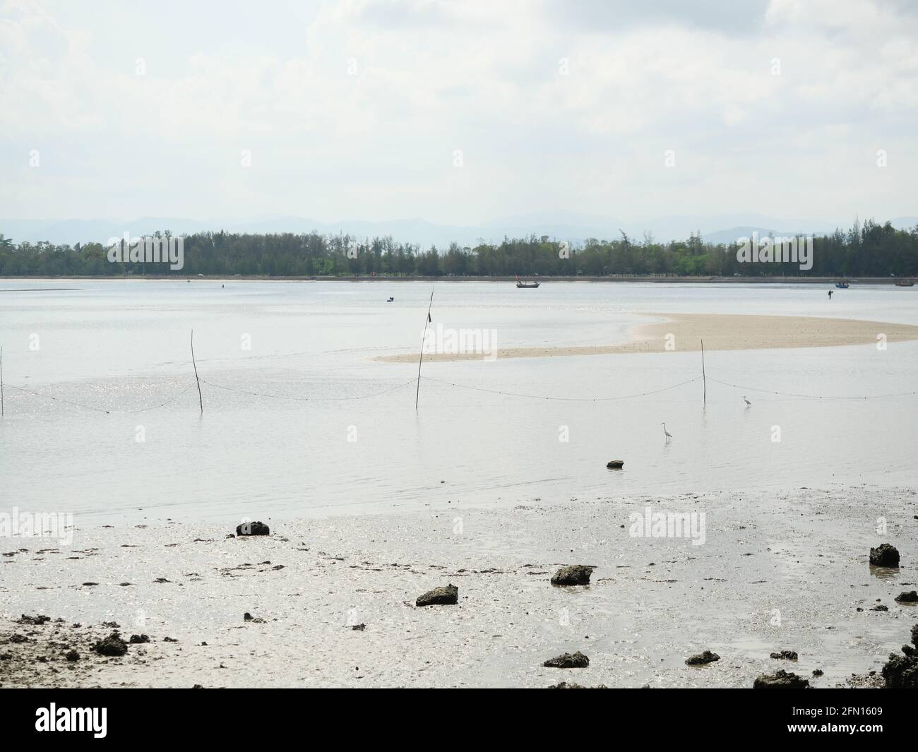 Scogliere rocciose con sabbia e fango in acqua fenomeno a bassa marea, pesca barca sulla spiaggia, onde oceaniche splash la riva severamente, Thailandia Foto Stock
