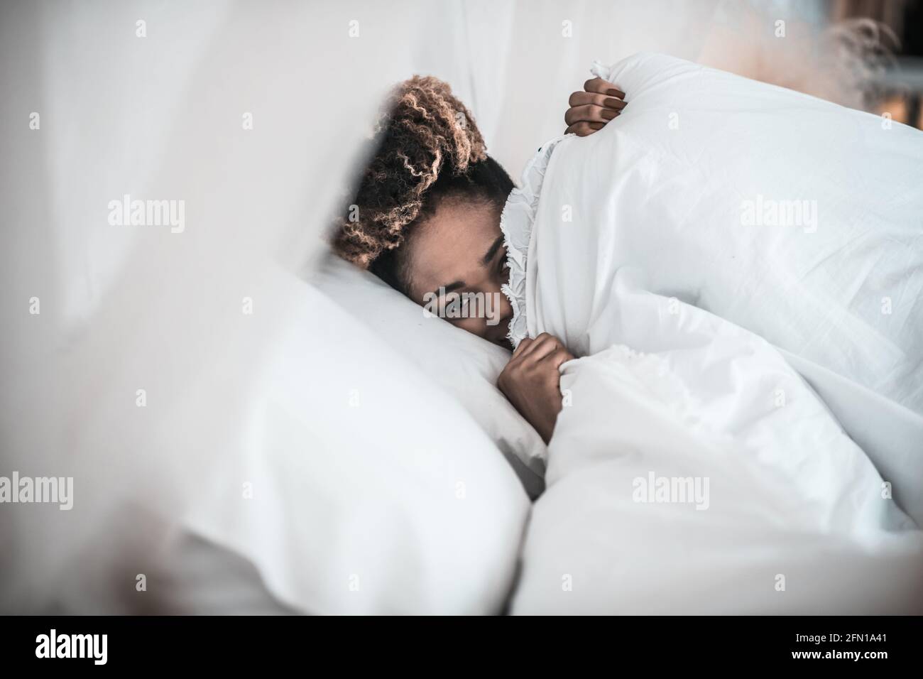 Donna assonnata che si sbirciava da sotto coperta Foto Stock