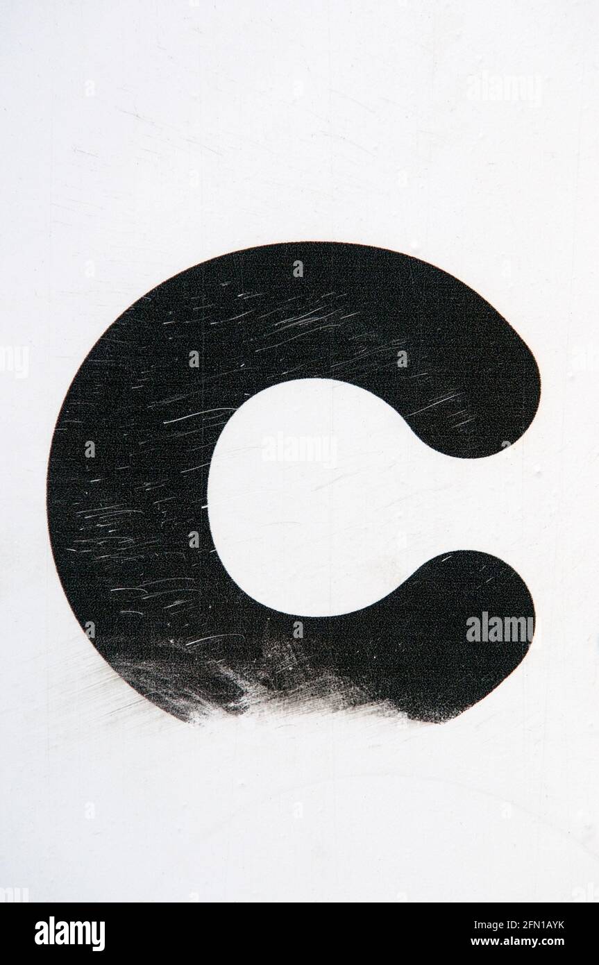Un primo piano di UNA lettera C nera usurata e intemperie su uno sfondo bianco Foto Stock