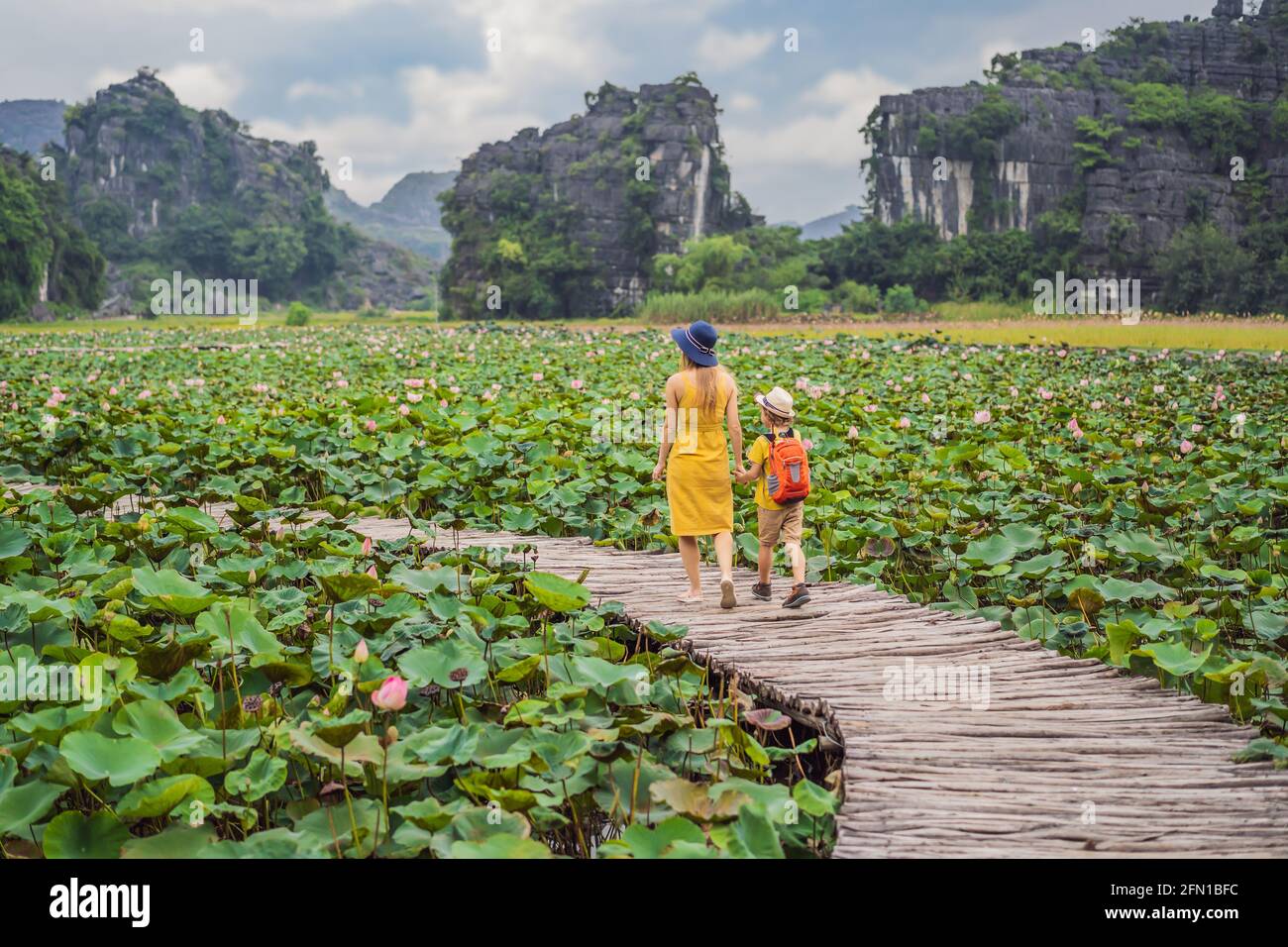 Madre e figlio in giallo sul sentiero tra il lago di loto. MUA Cave, Ninh Binh, Vietnam. Il Vietnam riapre dopo la quarantena Coronovirus COVID 19 Foto Stock