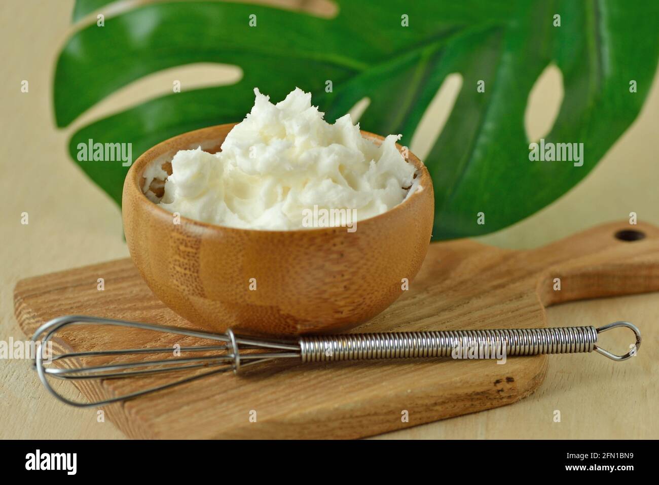 Crema viso composta da burro di karité e olio di argan recipiente in legno con frusta su piccola tagliere Foto Stock