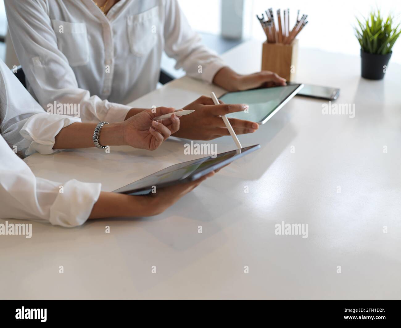 Riprese tagliate di mani femminili utilizzando tablet digitali mentre si è seduti l'uno accanto all'altro nella libreria Foto Stock