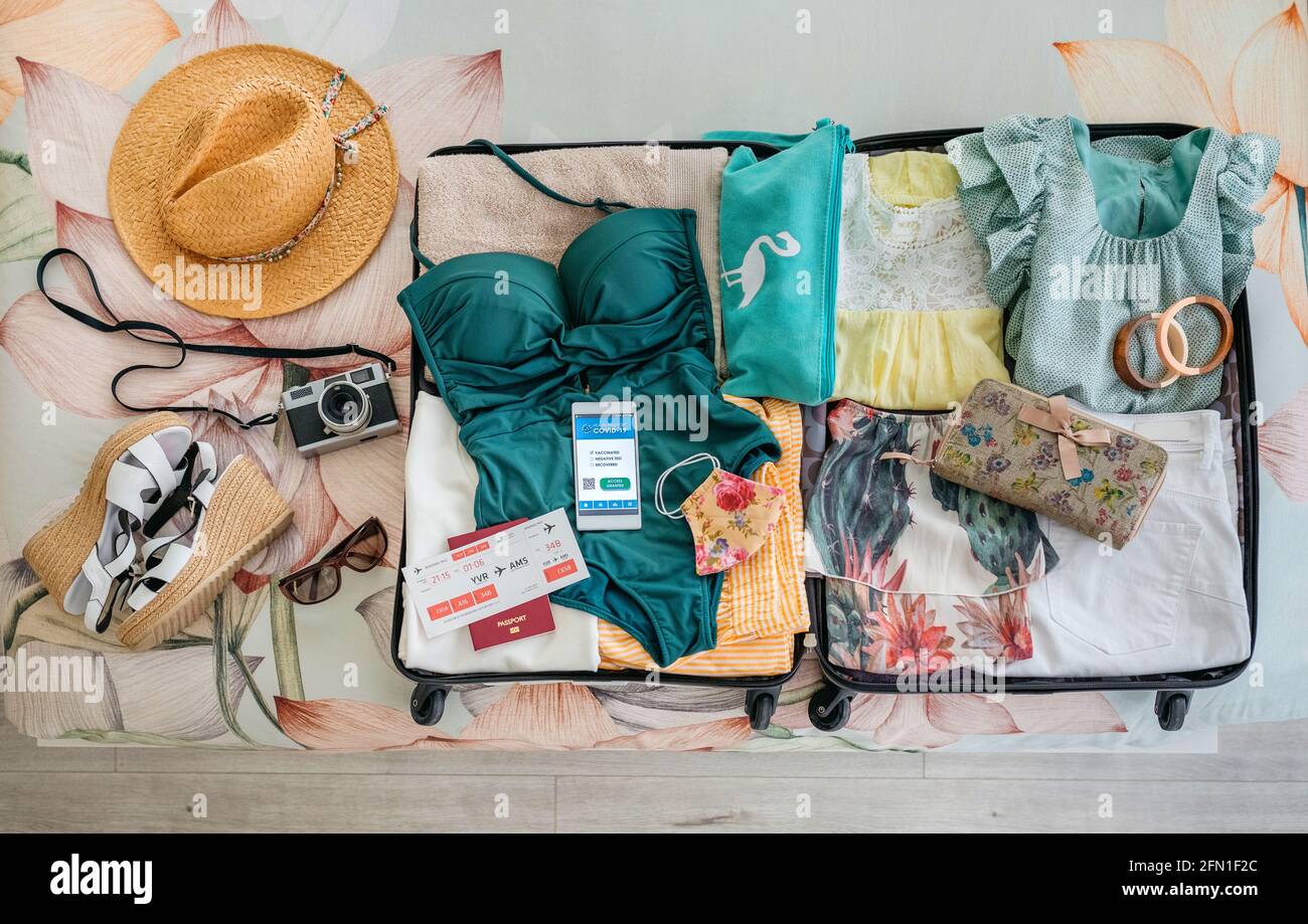 Valigia aperta con bagaglio da donna per vacanze in spiaggia e digitale passaporto sanitario Foto Stock