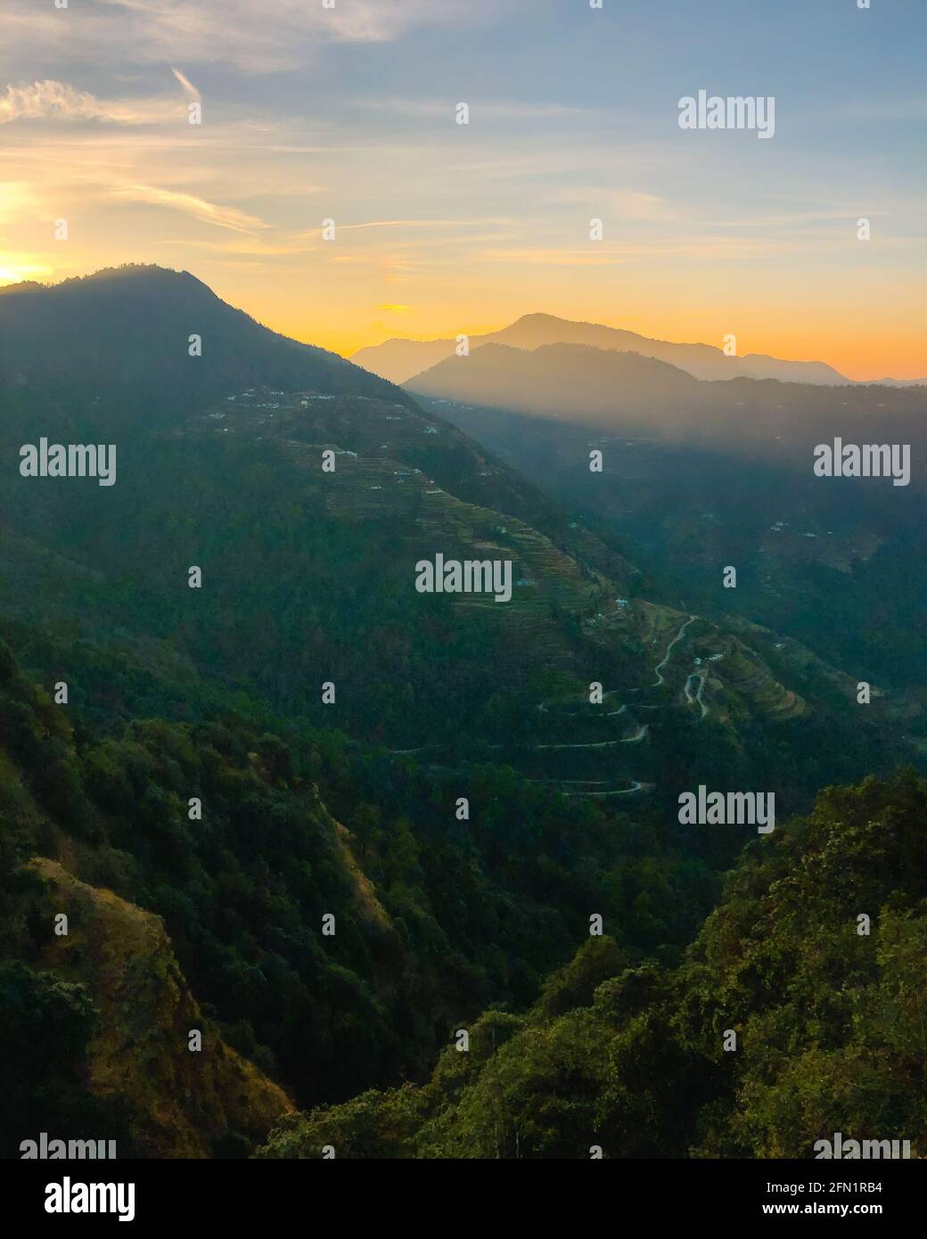 Bellissima alba dietro le colline. Raggi di sole che brillano sui villaggi sulle pendici delle montagne. Cielo drammatico. Foto Stock