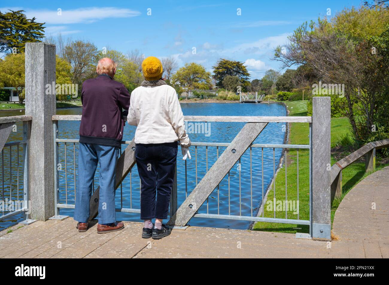 Coppia anziana o anziana in piedi su una piattaforma in un lago godendo la vista in una soleggiata giornata di primavera a Mewsbrook Park, Littlehampton, Inghilterra, Regno Unito. Foto Stock