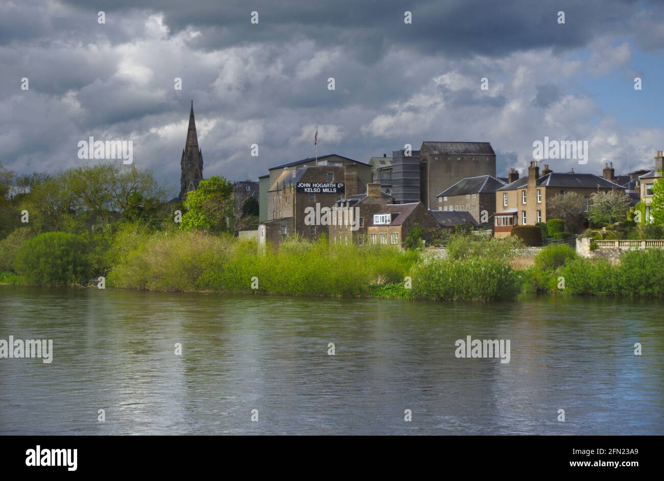 Vista sul fiume Tweed di Kelso sotto un cielo minaccioso, con John Hogarth Ltd Kelso Mills e Kelso North Parish Church sullo sfondo. Foto Stock