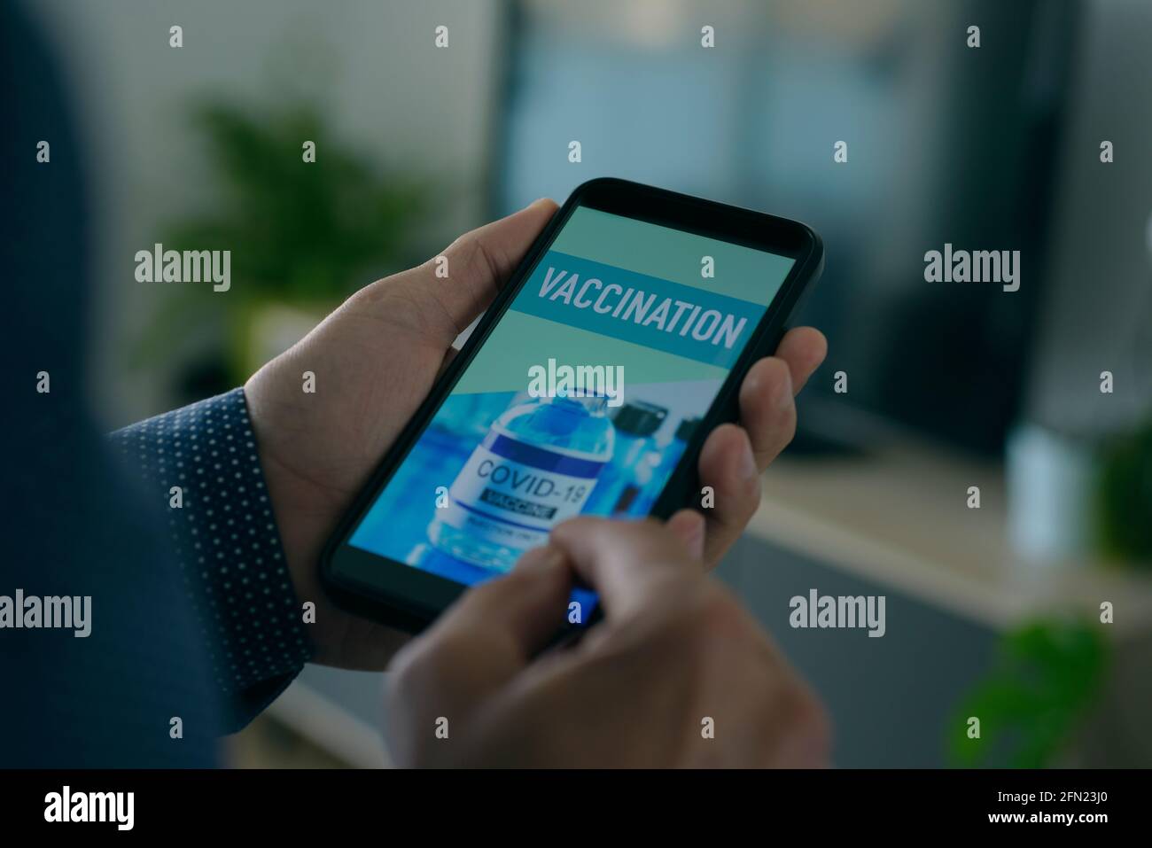 un giovane caucasico, seduto nel suo salotto, guarda il suo smartphone, che legge il testo della vaccinazione nel suo schermo Foto Stock