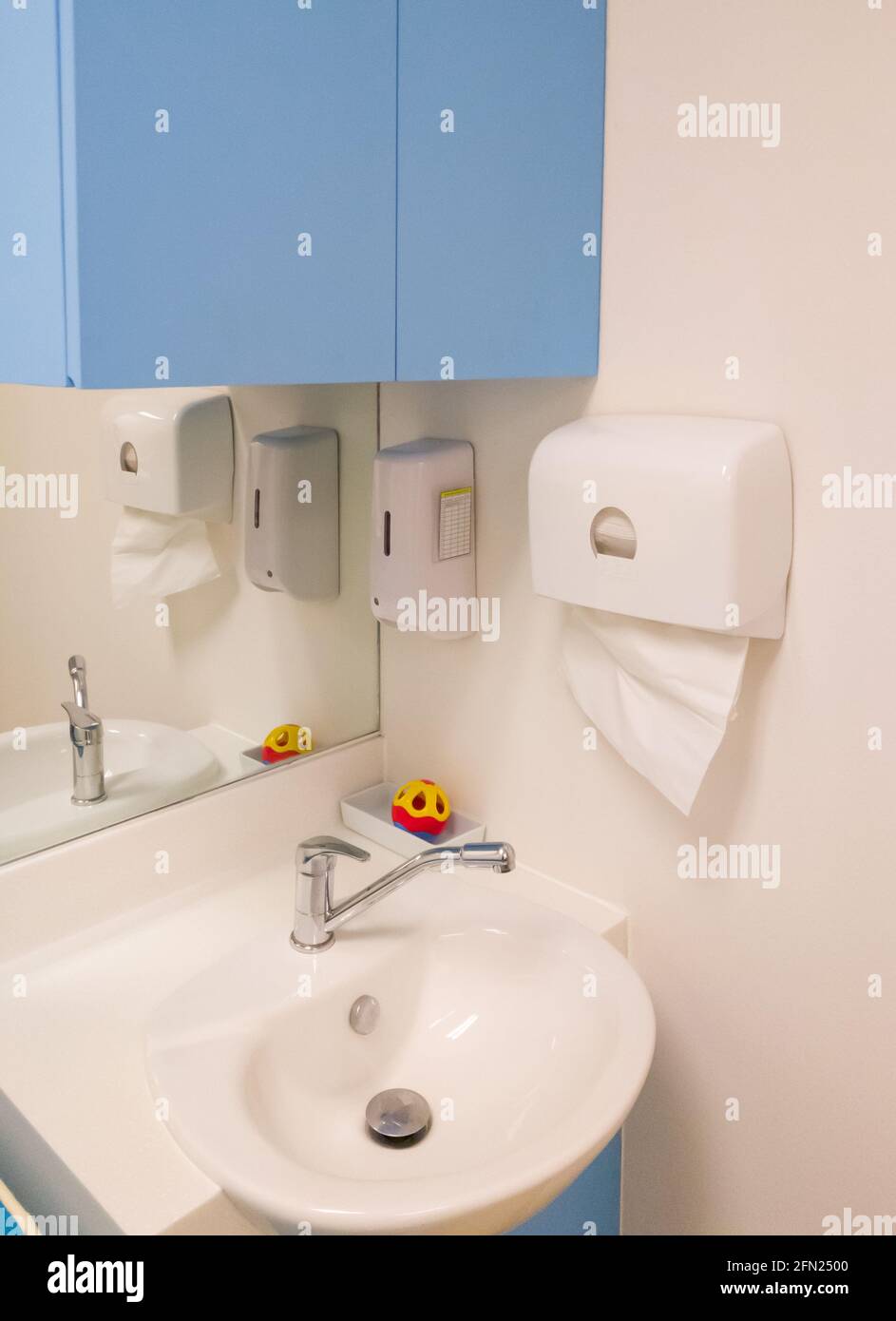 La mano pulita lava il lavabo con il dispenser di sciope e la cassetta di carta asciugamani vicino all'angolo della sala di visita medica nel moderno ospedale, da Foto Stock