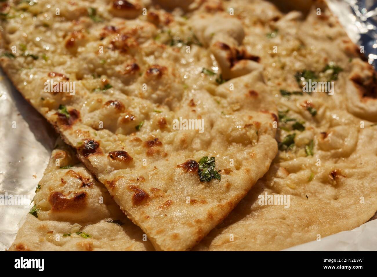 Spicchi di aglio naan, il classico pane indiano seduto su un involucro di foglio da asporto Foto Stock