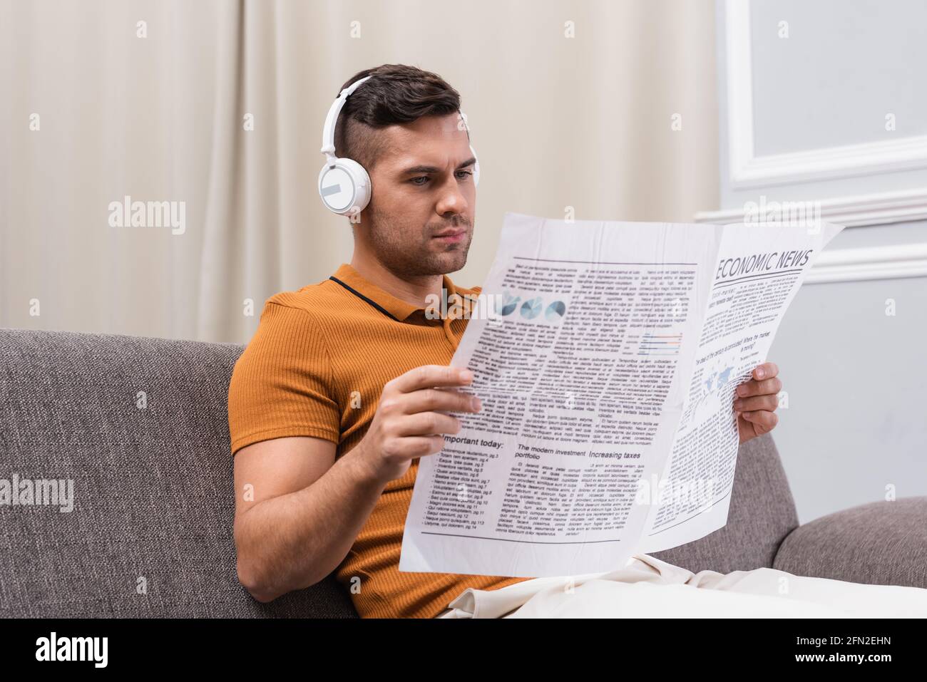 giovane uomo che legge il giornale mentre ascolta la musica con le cuffie wireless Foto Stock