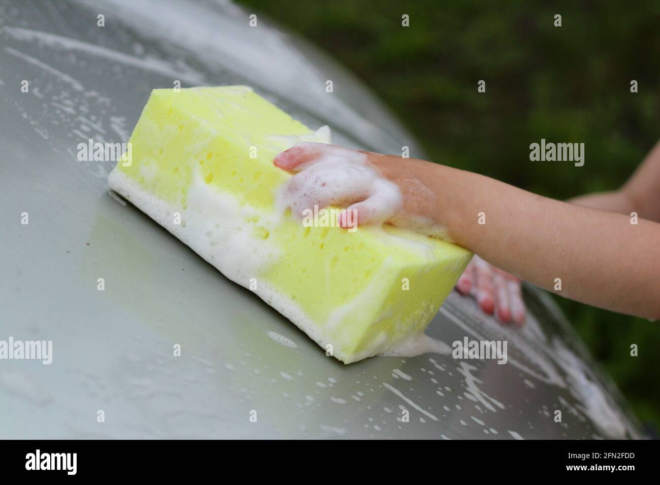 La mano dei bambini con una spugna gialla con schiuma lava il auto Foto Stock