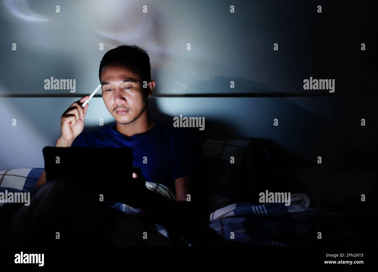 uomo che usa il tablet per leggere a letto e spegnere le luci prima di dormire a occhi chiusi. lavoro a letto Foto Stock