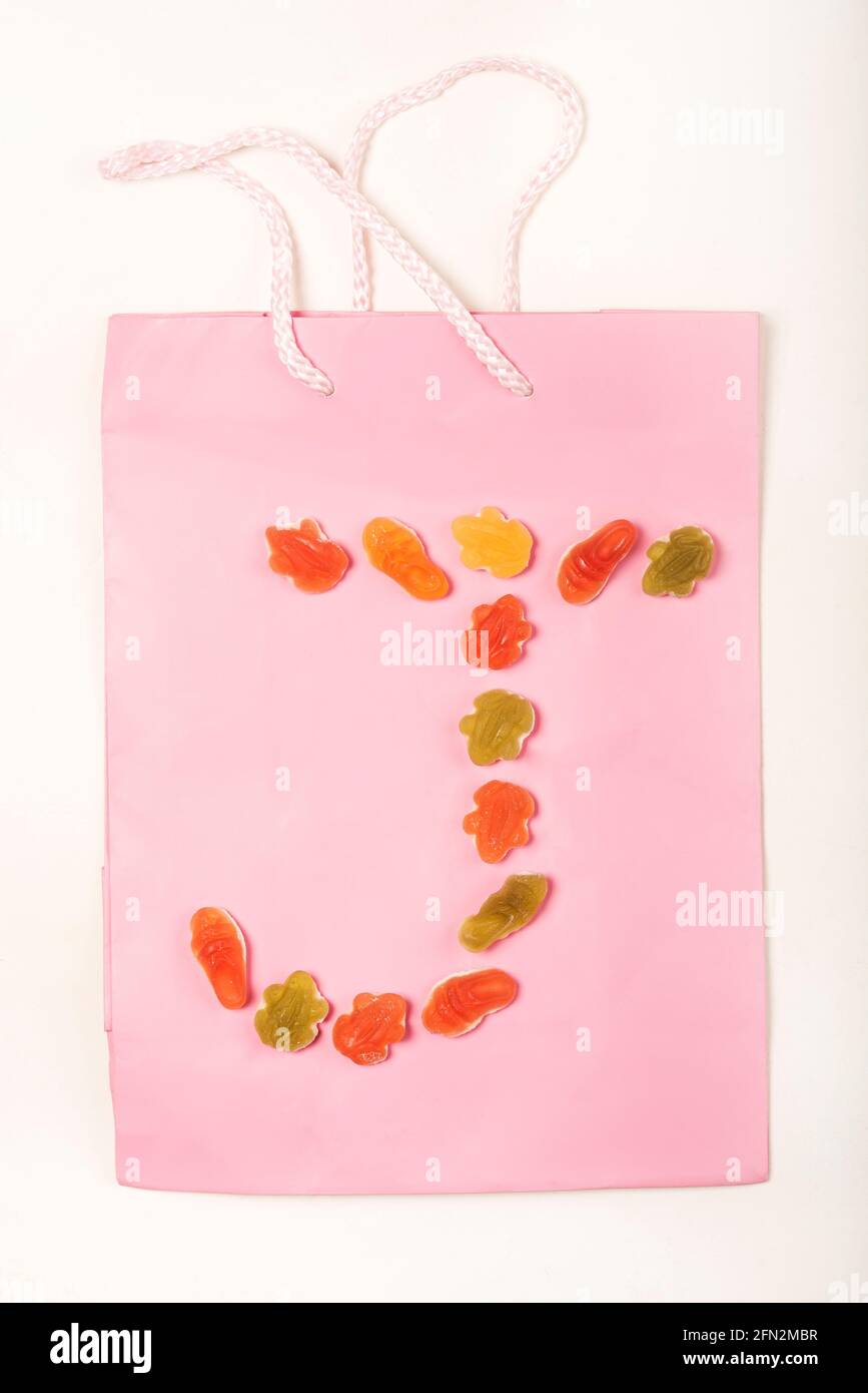 Lettere colorate a forma di alfabeto realizzate con una disposizione di dolci (caramelle) su una borsa regalo rosa, su sfondo bianco. Foto Stock