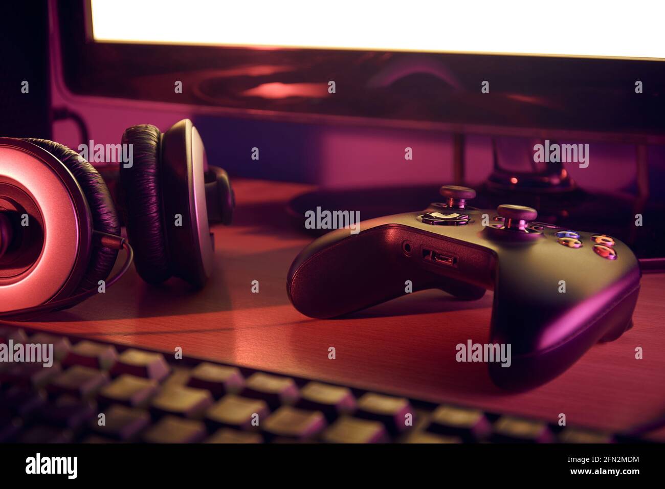 Visualizzazione della configurazione della scrivania di gioco con gamepad nero, cuffia, tastiera e monitor illuminati da luci rosse e viola. Foto Stock