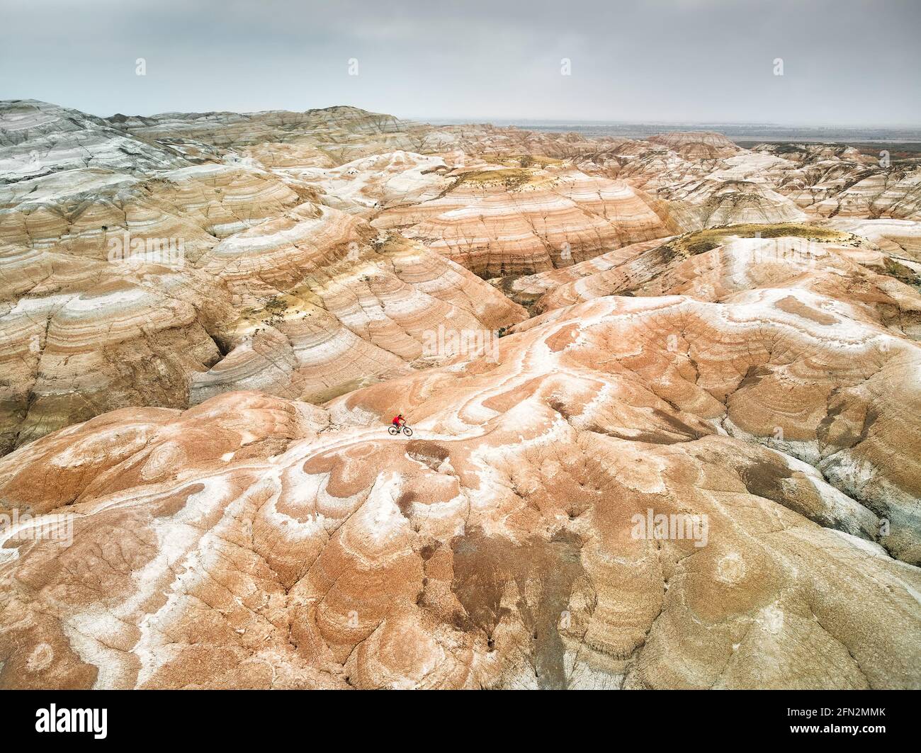 Drone aereo colpo di uomo che cavalcano la sua bicicletta sulla cima di surreale strisce rosso e bianco deserto montagna massiccio in Kazakhstan. Ricreazione e sano Foto Stock