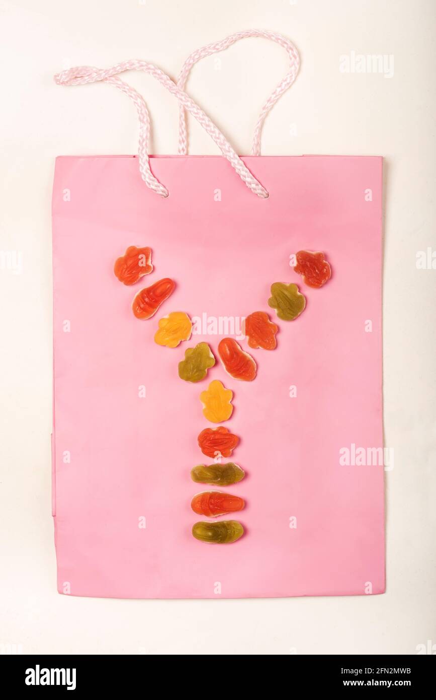 Lettere colorate a forma di alfabeto realizzate con una disposizione di dolci (caramelle) su una borsa regalo rosa, su sfondo bianco. Foto Stock