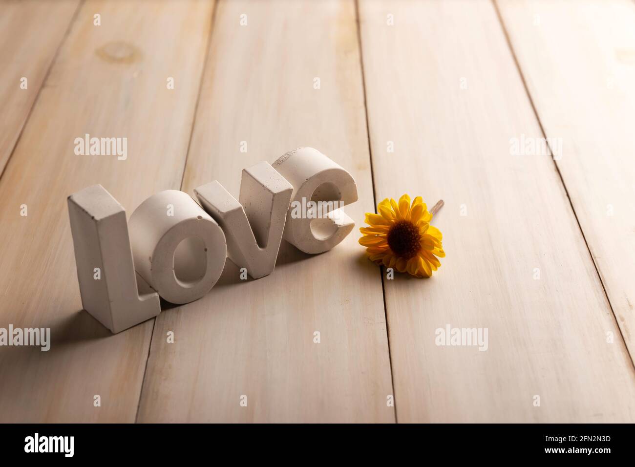 Immagine concettuale di lettere concrete che dicono amore con un giallo fiore su tavola di legno bianca lavata con spazio di copia Foto Stock