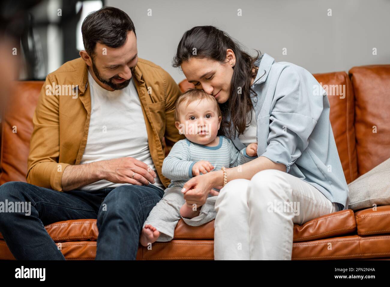 Il padre felice, la madre ed il figlio piccolo stanno giocando sul divano nel soggiorno. Cura del bambino e parenting. Amore e armonia nei rapporti familiari. Foto Stock