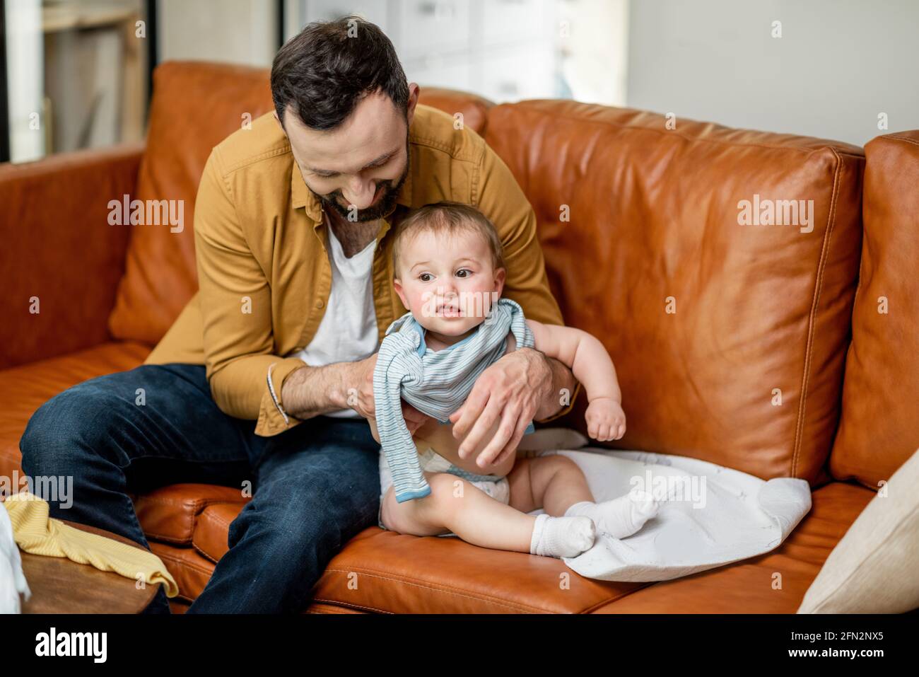 Padre che cambia vestiti al suo bambino figlio solo a casa. Baby sitter papà e paternità difficile. Foto Stock