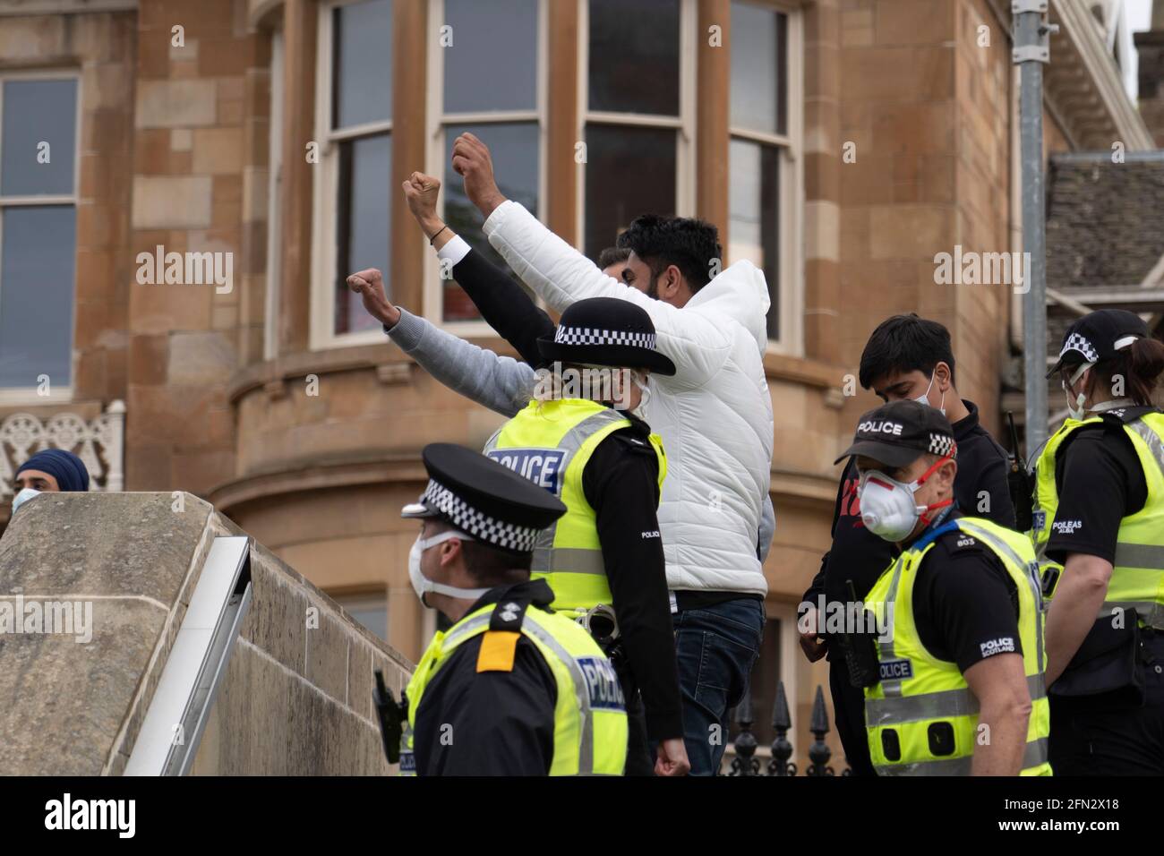 Glasgow, Scozia, Regno Unito. 13 maggio 2021. Alle ore 5.30 circa la polizia ha rilasciato due uomini da un veicolo di detenzione per ufficio a casa. Accompagnato dall'avvocato Aamer Anwar, gli uomini camminarono verso una vicina moschea circondata da centinaia di polizia e sostenitori che in precedenza avevano circondato il veicolo e sedevano sulla strada.due maschi e Aamer Anwar camminano su gradini di moschea per rivolgersi ai sostenitori. Credit: Iain Masterton/Alamy Live News Foto Stock