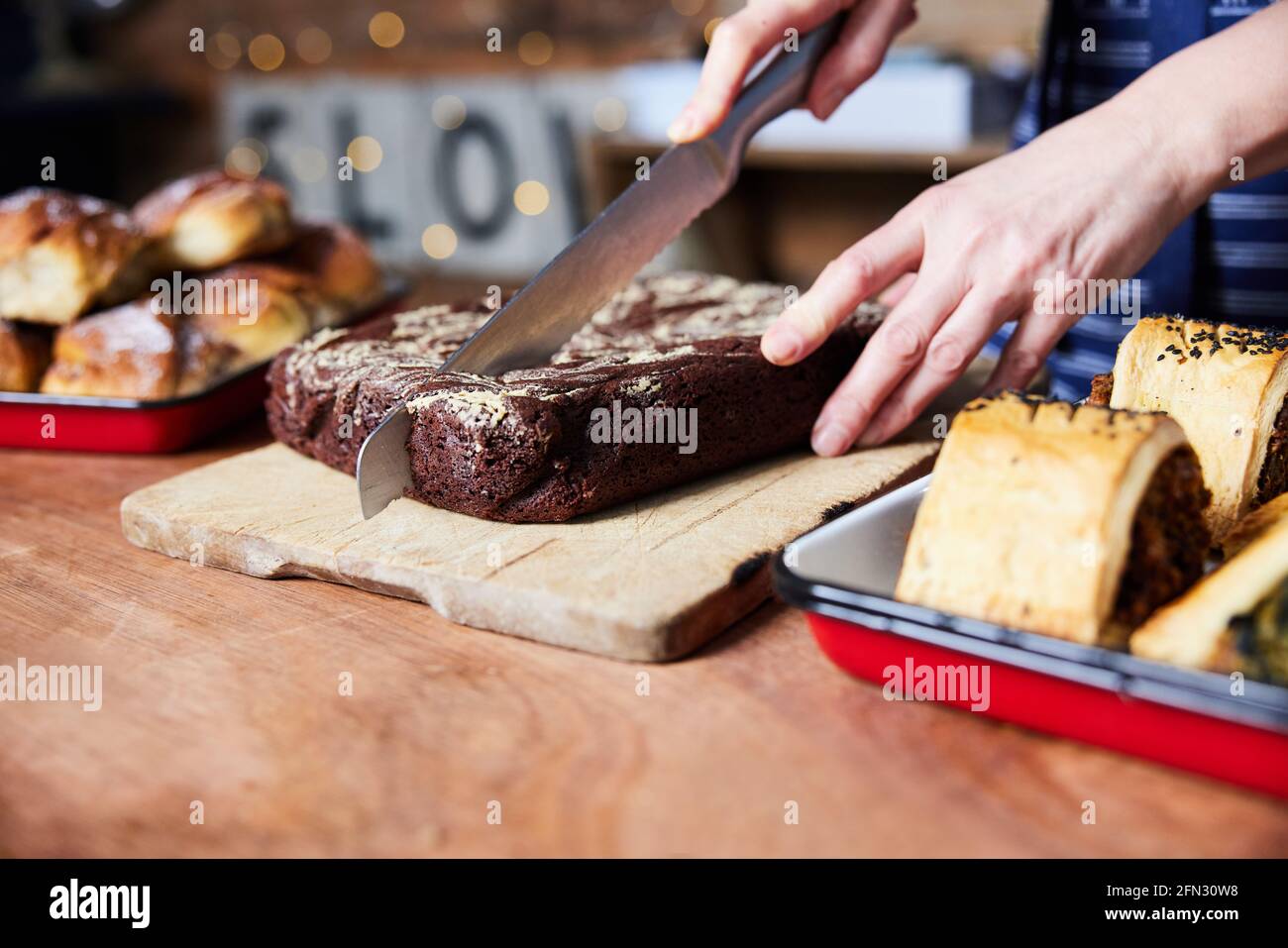 Assistente vendite in panetteria che taglia Brownies appena sfornati su Contatore Foto Stock