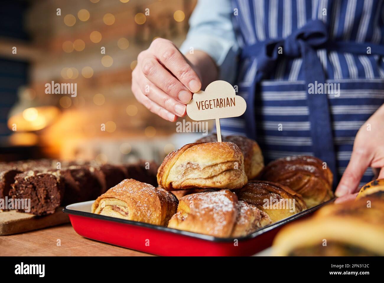 Assistente vendite in panetteria che mette Vegetarian Free Label in fresco Panino alla cannella al forno Foto Stock