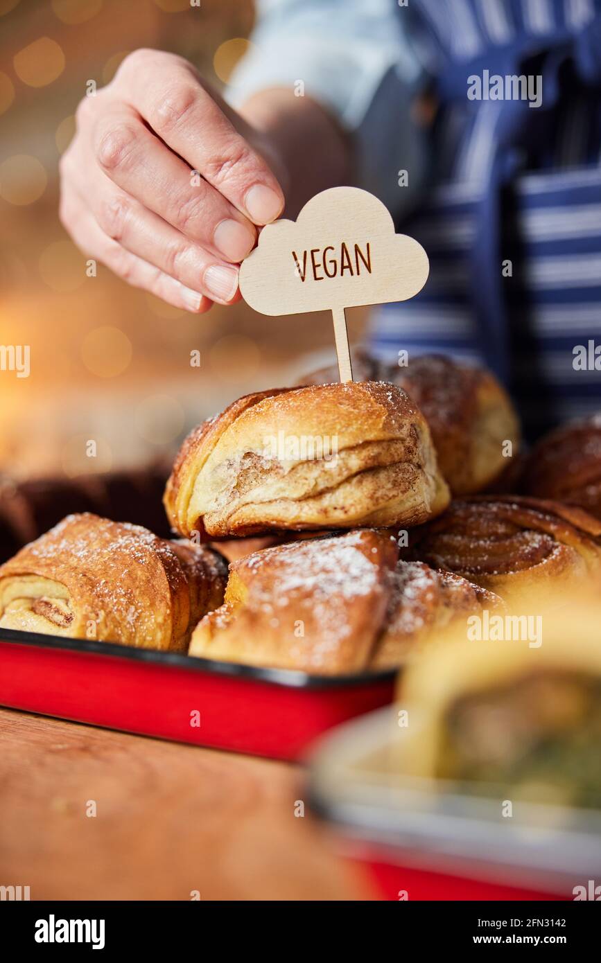 Assistente vendite in panetteria mettendo Vegan Label in appena sfornato Ciambelle di cannella Foto Stock