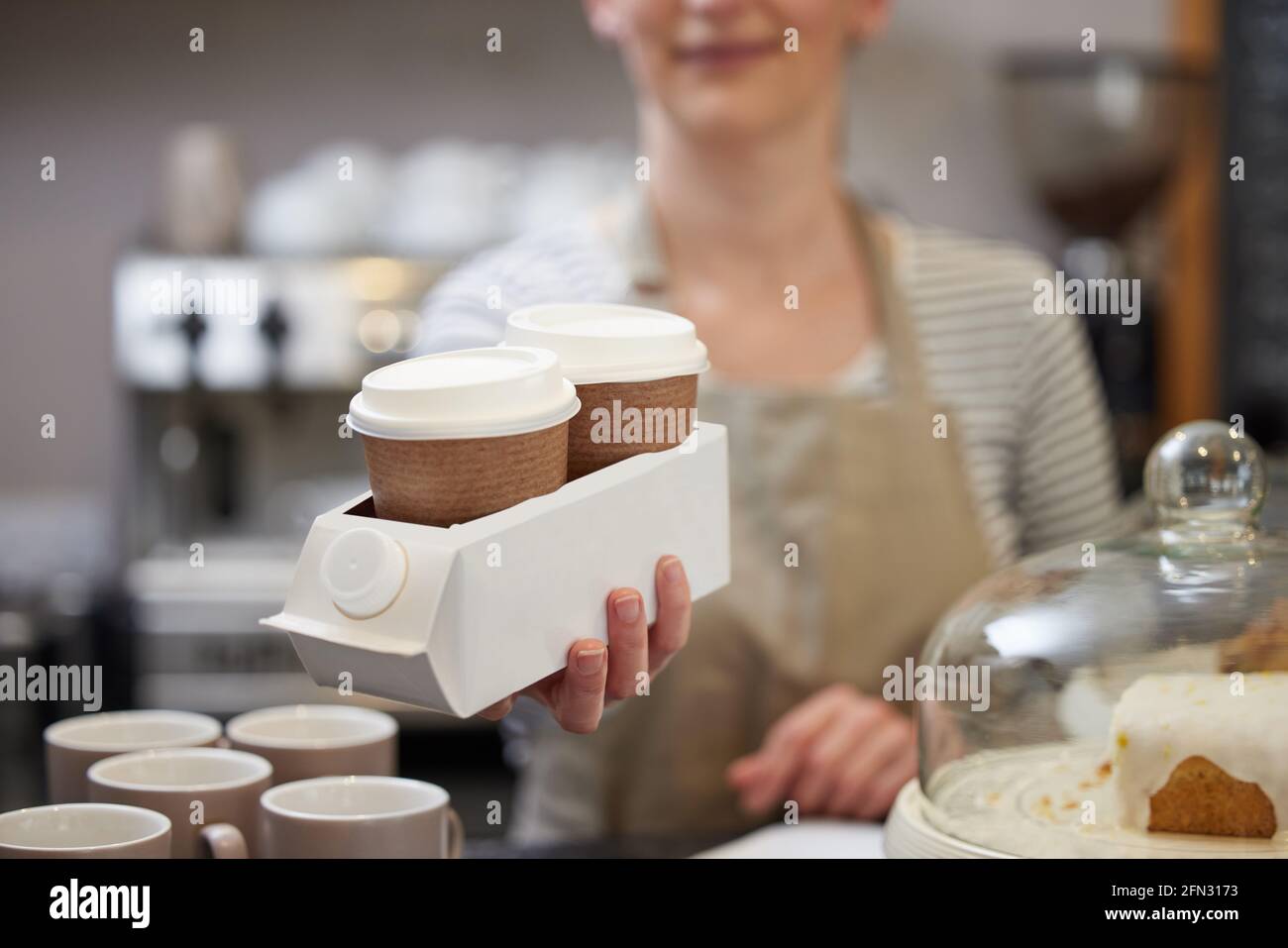 Primo piano di Female Worker in Cafe che serve caffè Takeaway In contenitore riciclato realizzato in cartone usato Foto Stock