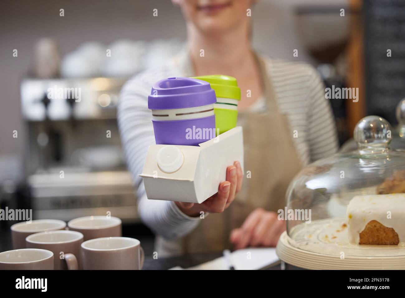 Primo piano di Female Worker in Cafe che serve caffè Takeaway In contenitore riciclato realizzato in cartone usato Foto Stock