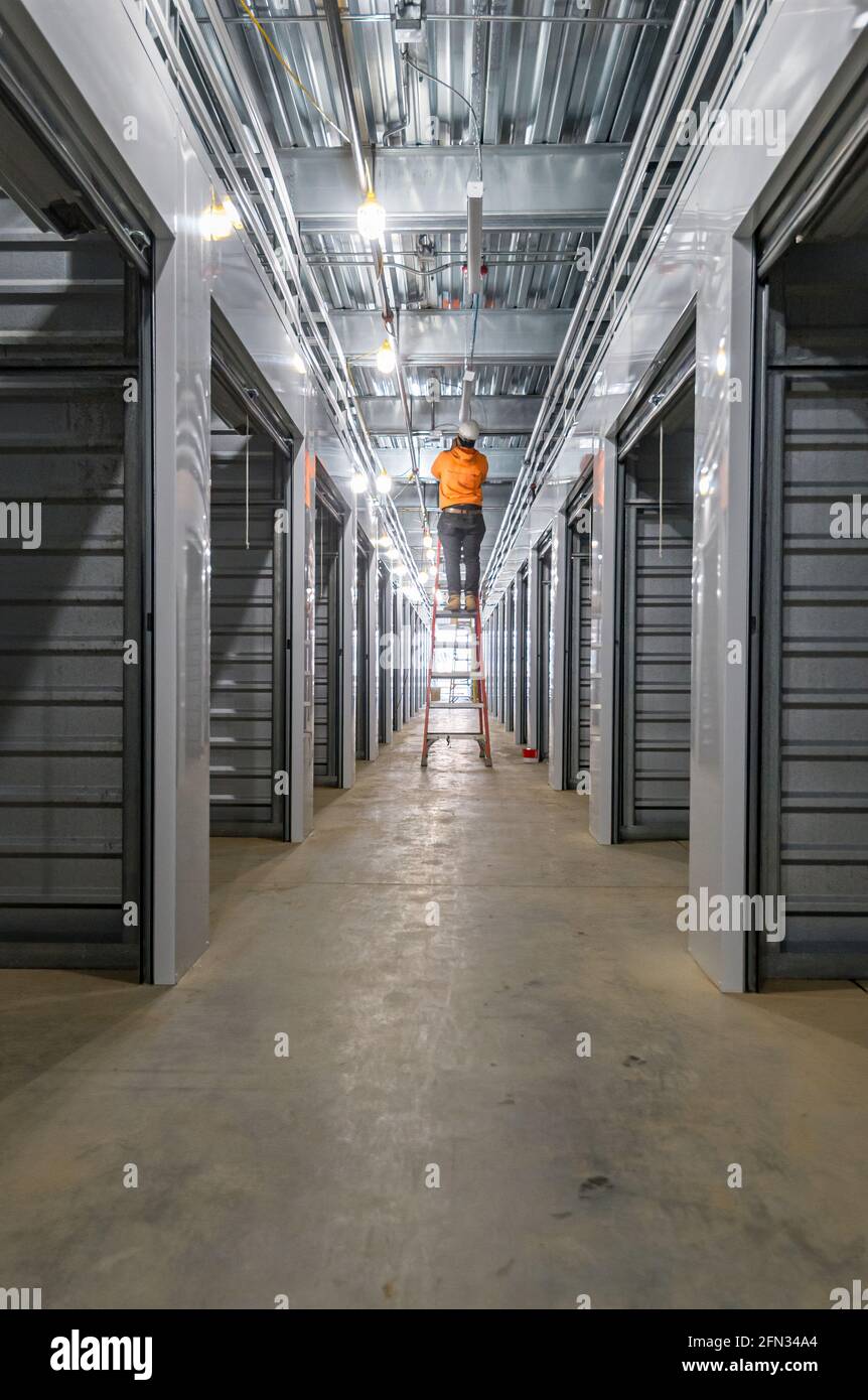 Elettricista addetto alla costruzione che alletta le luci sulla scala all'interno dell'edificio commerciale in costruzione. Foto Stock