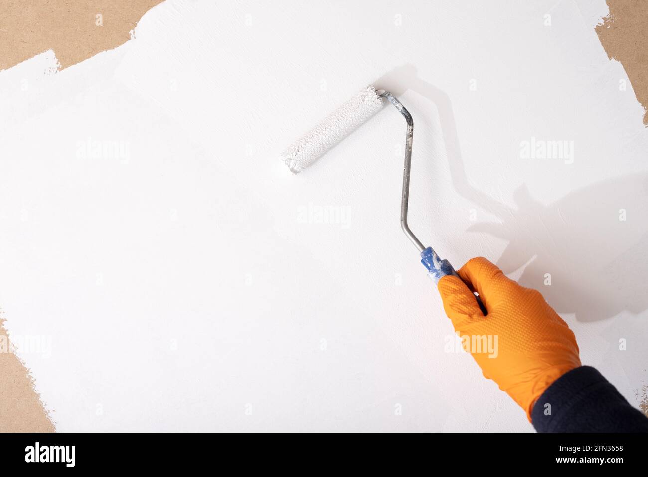 Mano in vernice guanto di protezione con vernice bianca una tavola di legno con rullo. Spazio di copia Foto Stock