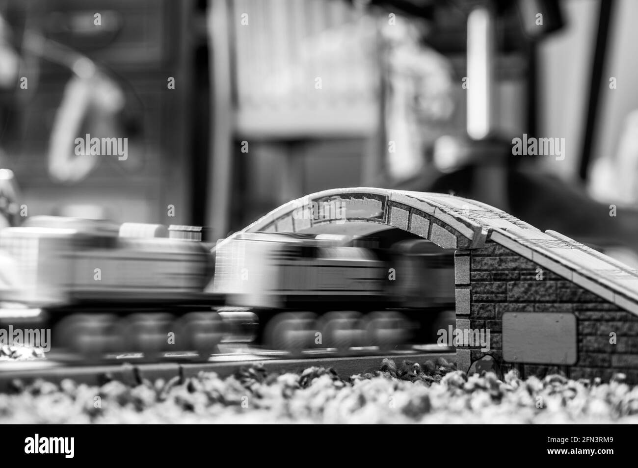 messa a fuoco selettiva sulla pista del treno giocattolo in legno con ponte sfocato e locomotiva in movimento in background Foto Stock