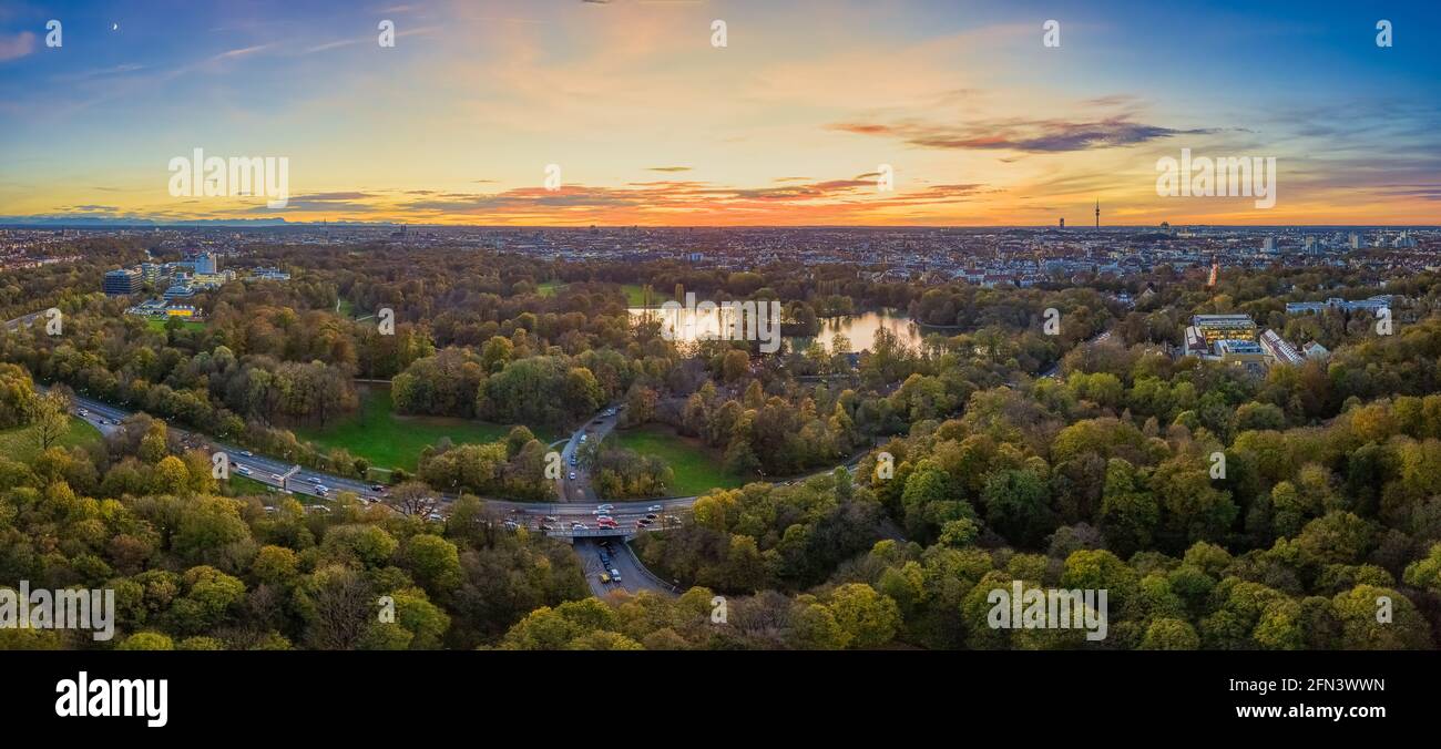 Vivido tramonto sul bellissimo giardino inglese di Munichs con le auto in primo piano e il verde popolare parco come il motivo principale nel middleground. Foto Stock