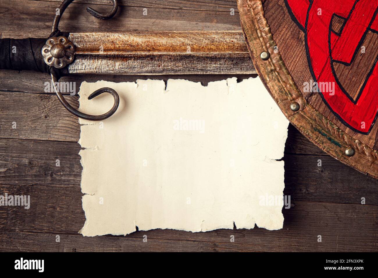 Vintage sfondo medievale con spada e scudo e foglio bianco di carta bianca o di cartoncino su tavola di legno ruvido Foto Stock