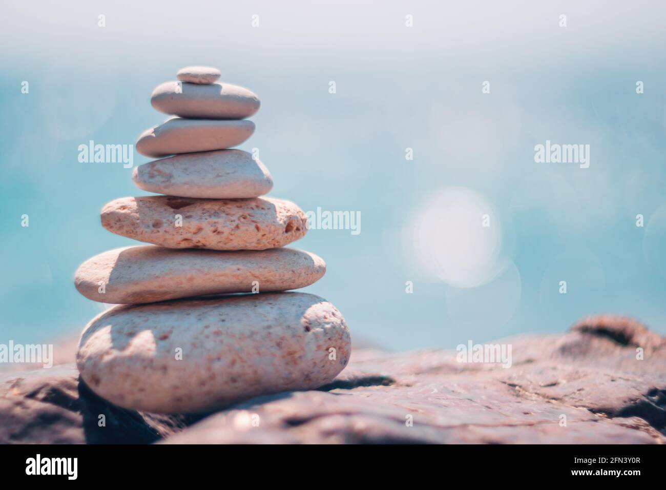 Equilibrata piramide di ciottoli sulla spiaggia in una giornata di sole. Abstract Sea bokeh sullo sfondo. Messa a fuoco selettiva. Pietre Zen sulla spiaggia di mare, meditazione Foto Stock