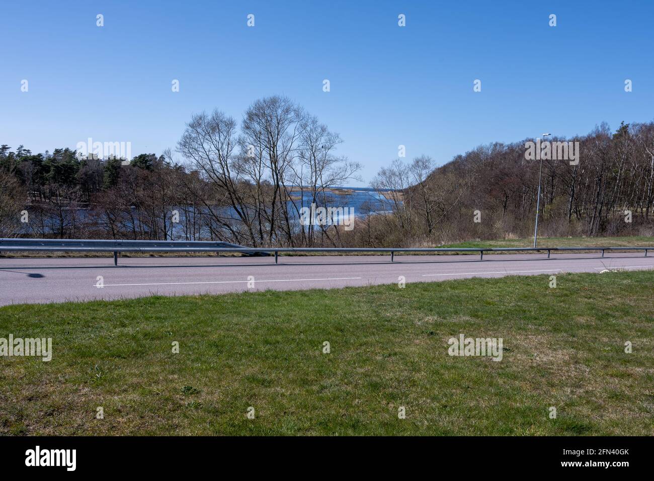 Un campo coperto di erba aperta con una strada e una bella baia blu oceano azur sullo sfondo. Foto di Laholm, Svezia Foto Stock