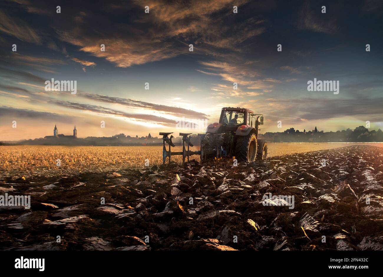 il trattore aratura il campo di sera al tramonto. Foto Stock