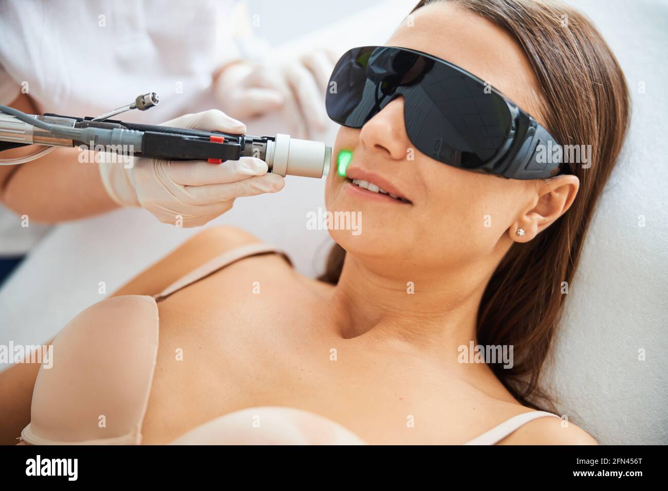 Donna che indossa occhiali di protezione durante la rimozione dei peli del viso Foto Stock