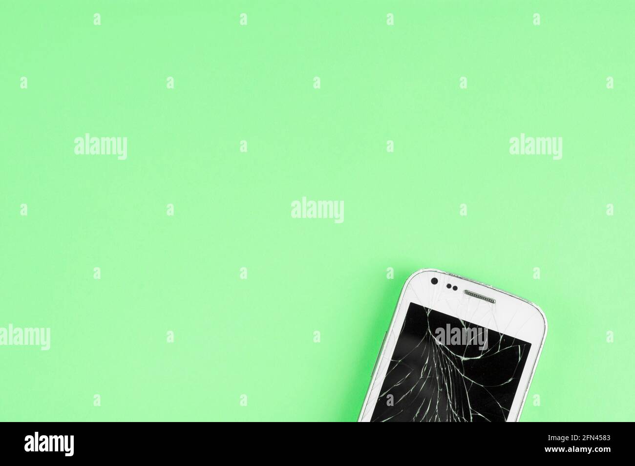 Un telefono cellulare touchscreen rotto su sfondo verde con copia spazio per il testo Foto Stock