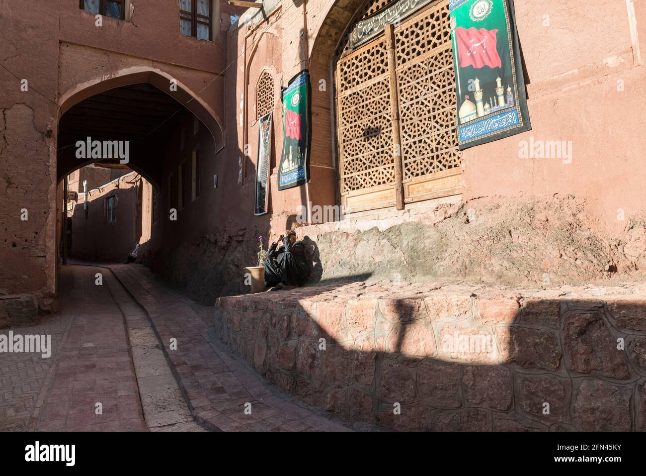 Maschio residente seduto contro un muro e godendo il sole di autunno nel villaggio antico Abyaneh, Provincia di Isfahan, Iran Foto Stock