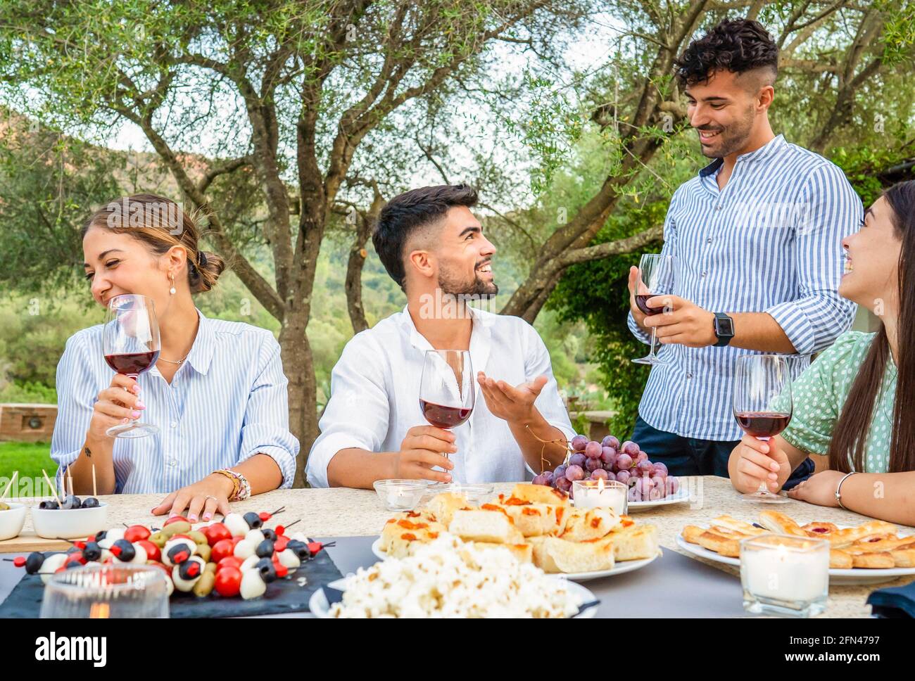 Festa tipica italiana per la vendemmia in casa di campagna. Gruppo di giovani amici riuniti a tavola con spuntini, pizza, pomodori e. Foto Stock