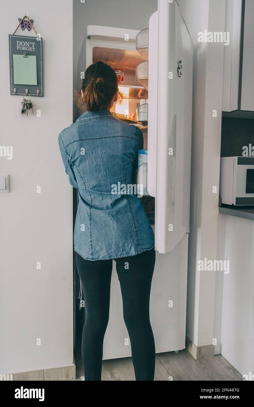 ragazza all'interno della cucina aprendo la porta del frigorifero e guardando interno Foto Stock