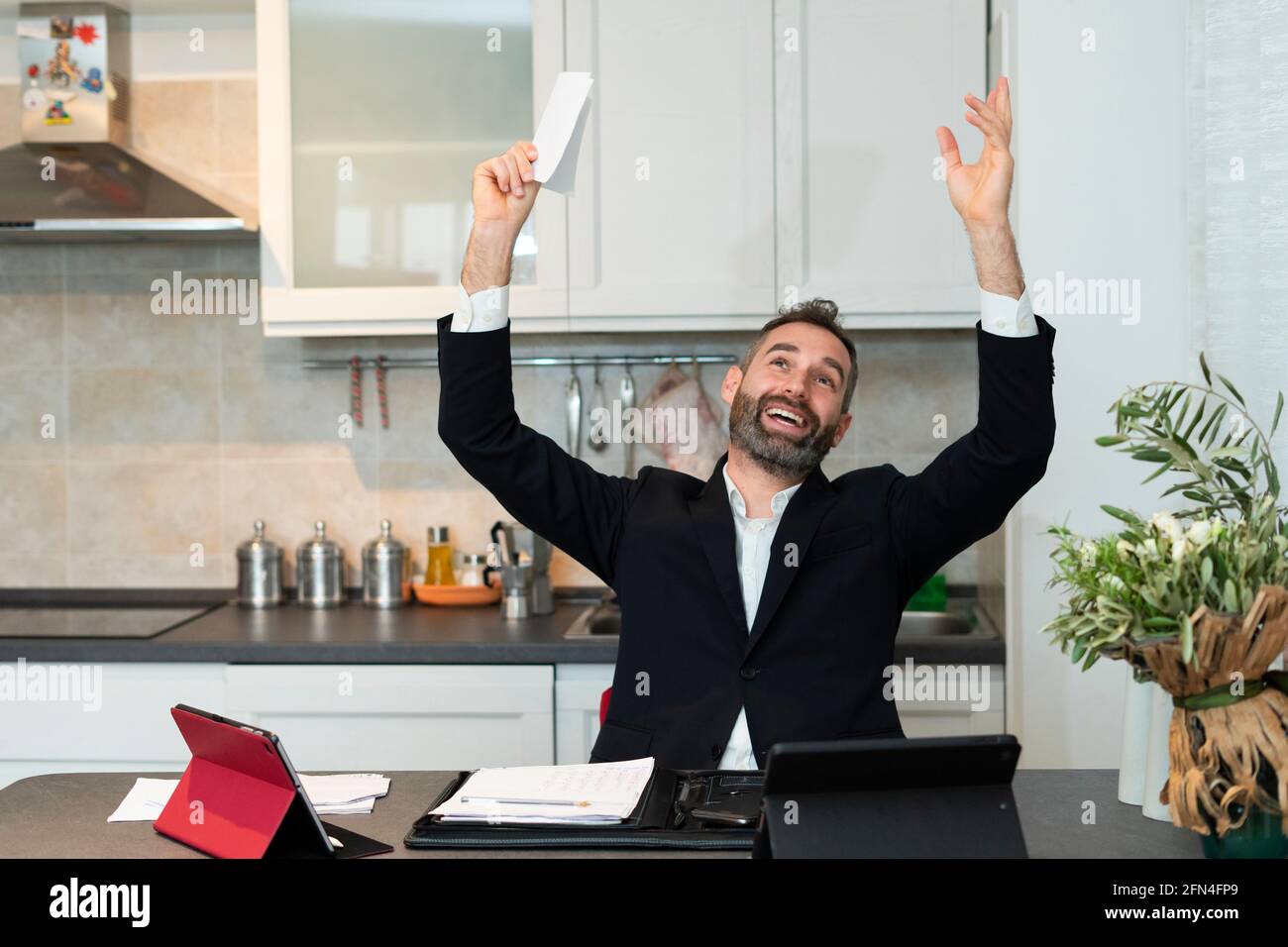 Ritratto di gioioso giovane uomo d'affari che alza entrambe le braccia per un affare all'alba. L'operaio domestico espressivo gioisce nella cucina. Riunione di successo. Foto Stock