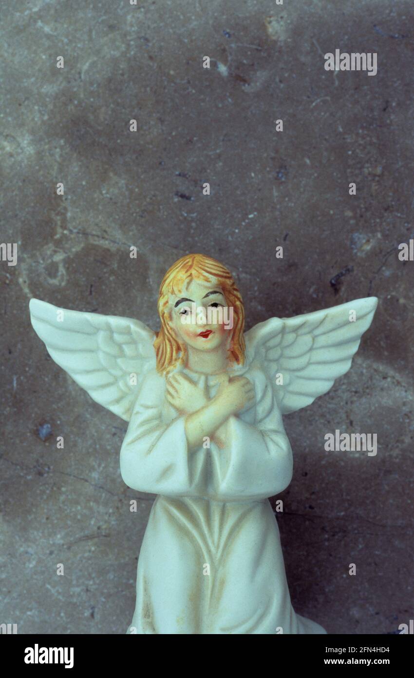 Modello in porcellana di angelo ragazza in abito bianco con capelli rossi e braccia incrociate inginocchiate davanti alla parete di marmo Foto Stock