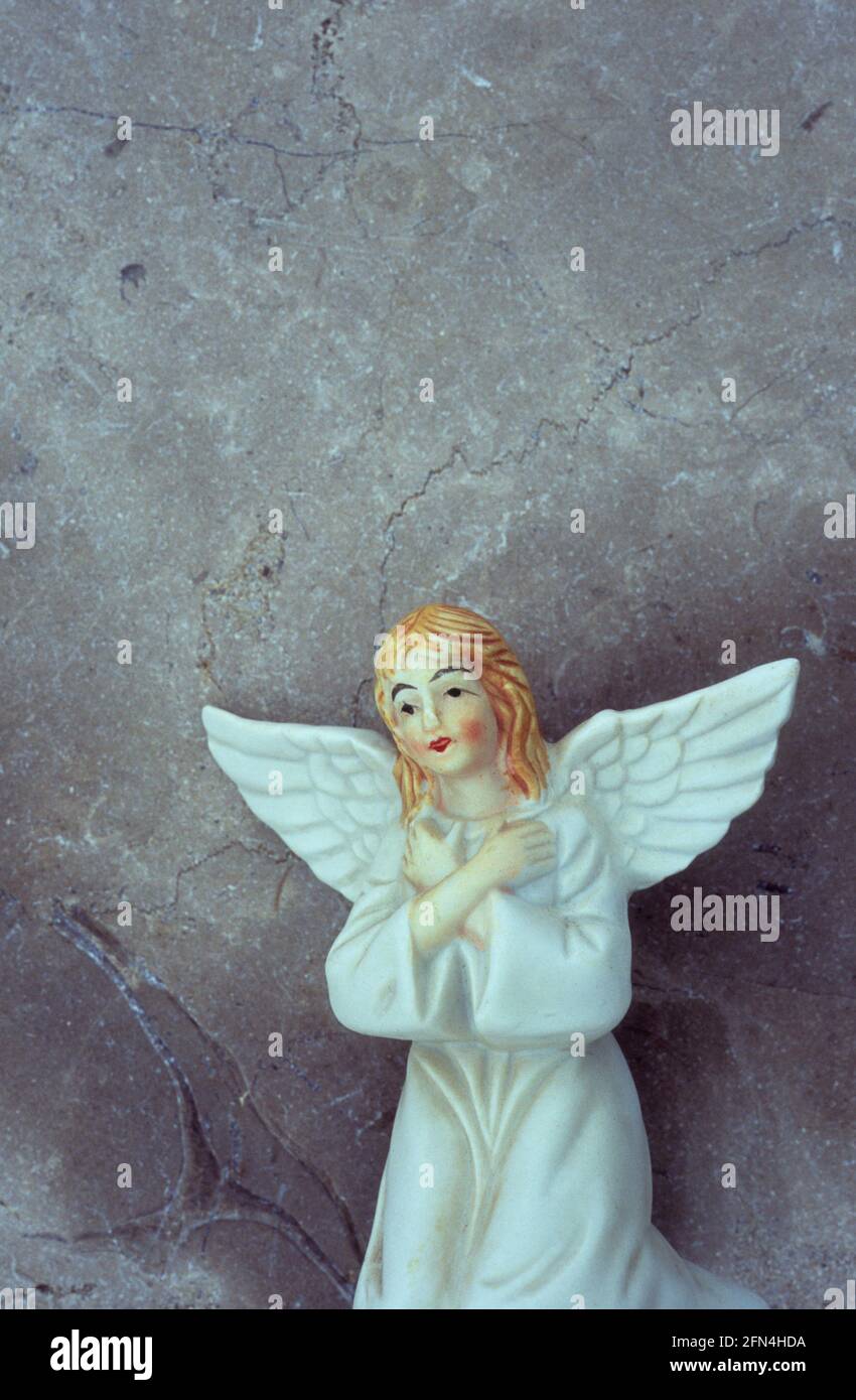 Modello in porcellana di angelo ragazza in abito bianco con capelli rossi e braccia incrociate inginocchiate davanti alla parete di marmo Foto Stock