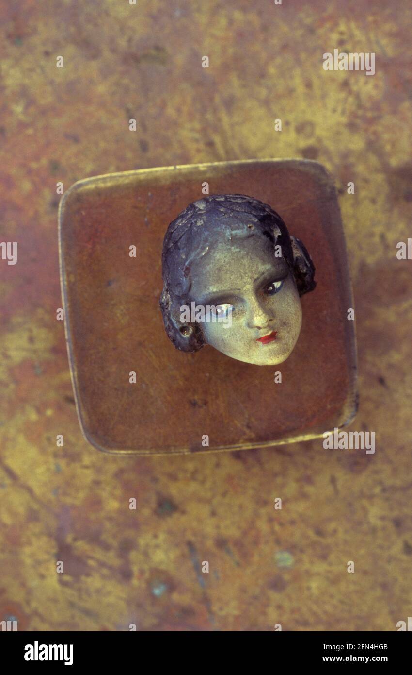 Testa della bambola degli anni '20 o ornamento con carnagione di olive e capelli neri giacenti su un piccolo contenitore di ottone Foto Stock